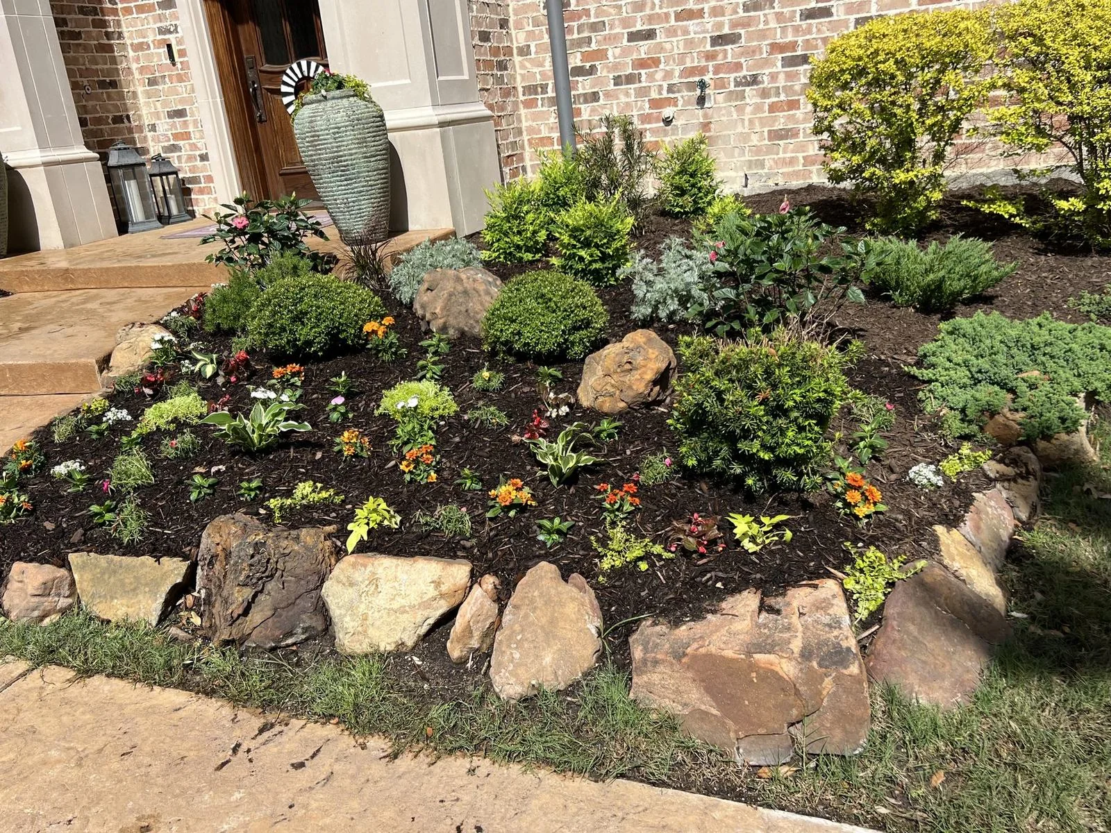 Freshly mulched garden bed by Frisco Landscapes in Plano, TX with boulders, shrubs, and seasonal plants