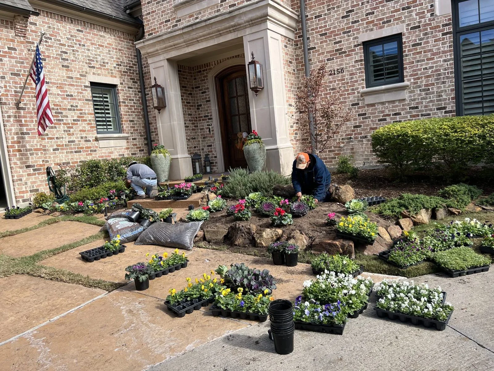 Frisco Landscapes crew planting seasonal flowers in a stone-edged front bed at a Plano, TX home